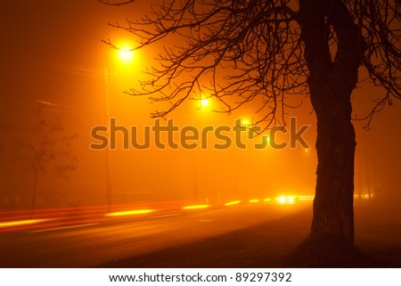 traffic on foggy road with automobile light streaks and tree