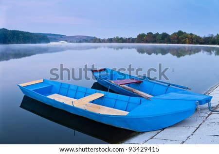 two blue boats on lake in morning light fog and forest with reflection