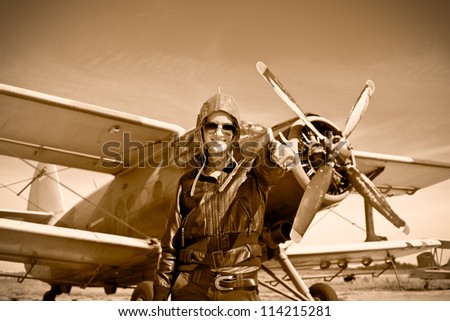 Portrait of beautiful female pilot with plane behind. Sepia photo.