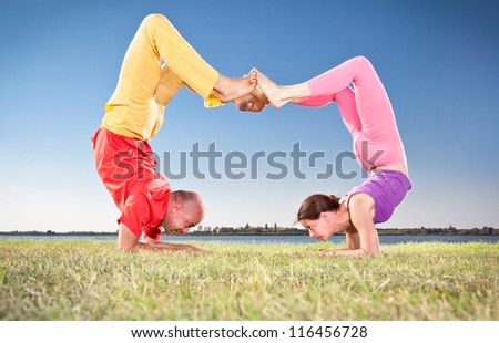 Yoga couple, man and woman doing Vrschikasana scorpion pose on lake bench. Yoga concept.
