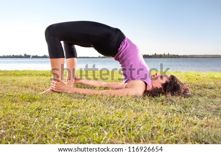 Beautiful young woman doing yoga exercise on green grass next to the  lake. Yoga concept.