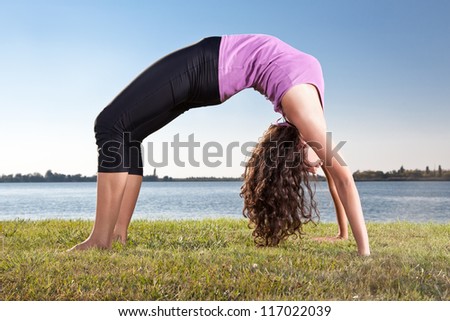 Beautiful young woman doing yoga exercise on green grass next to the lake. Yoga concept.