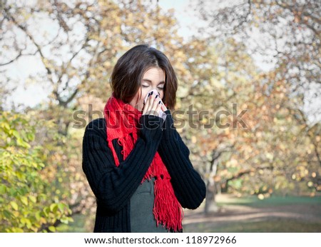 Caucasian woman with cold sneezing into tissue in autumn park