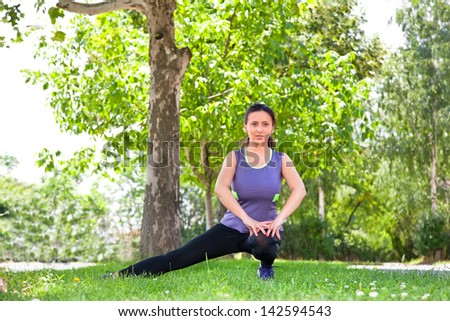 Exercise woman stretching hamstring leg muscles during outdoor running workout. Smiling happy sport fitness model in city park.
