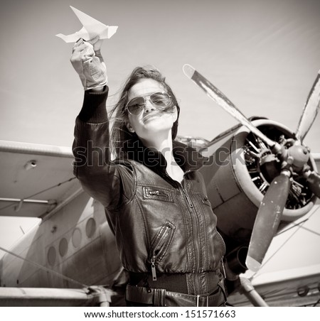 Portrait of young beautiful woman pilot in front of  airplane.