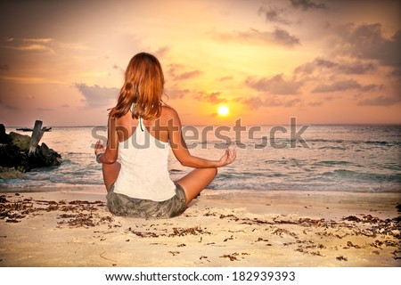 A relaxed sexy young brunette woman sitting on a deserted tropical beach at sunset
