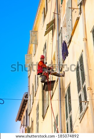 NICE, FRANCE- MARCH 24, 2014: Worker carries severe altitude jobs hanging by a leash on the exterior facade on March 24, 2014. in Nice, France.