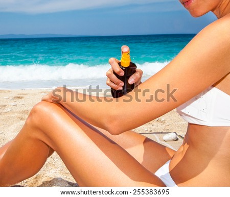 Woman applying suntan lotion from a spray bottle . Greece.