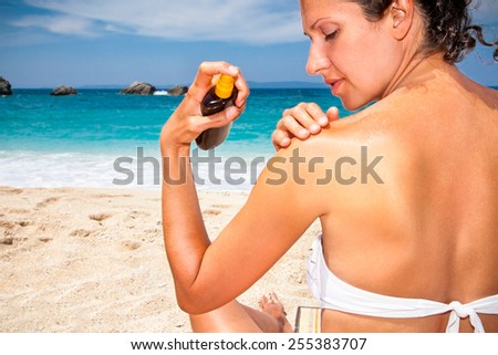 Woman applying suntan lotion from a spray bottle . Greece.