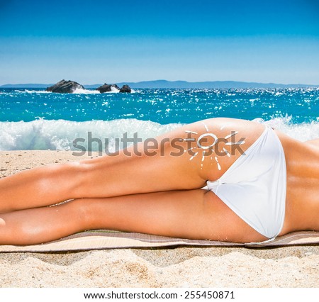 Beach vacation. Hot beautiful woman with sun sign in bikini lying on the beach. Greece.