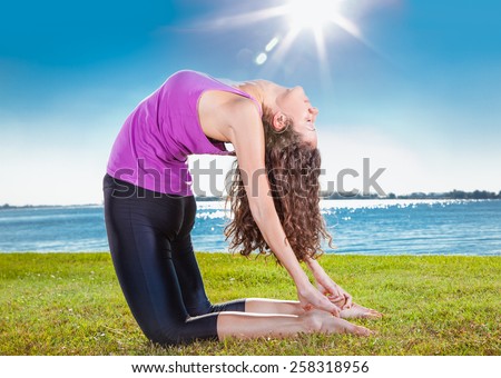 Beautiful young woman doing yoga exercise on green grass next to the  lake. Yoga concept.