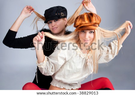 Portrait of two beautiful women hold hair and wearing retro caps, studio shot