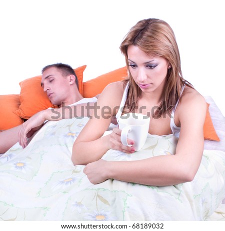 Young sad man sitting on bed, nearby unsatisfied woman. Focus on the man.