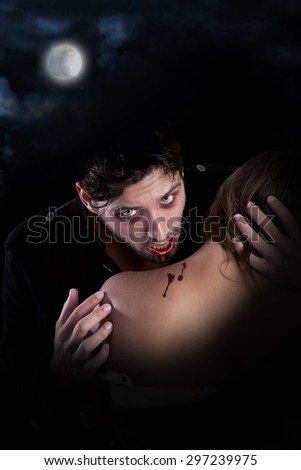 handsome vampire biting girl isolated in dark background