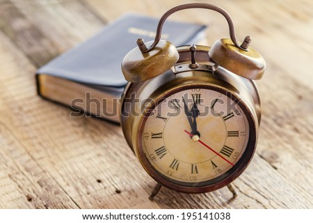 Clock and Bible on wood. Concept of clock showing a few minutes to twelve o\'clock. Focus on the clock.