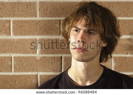 A young man in front of a brick wall in the afternoon sun