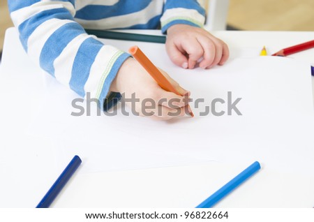 Toddler draws with an orange pencil