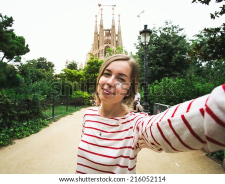 Happy beautiful young woman tourist smiling and taking selfie self-portrait in front of Sagrada Familia while traveling in Barcelona, Spain.