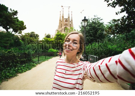 Happy beautiful young woman tourist smiling and taking selfie self-portrait in front of Sagrada Familia while traveling in Barcelona, Spain.