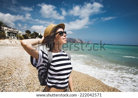 Young beautiful woman at the beach enjoying the summer, standing in a sun hat at the beach with face raised to the sunlight.