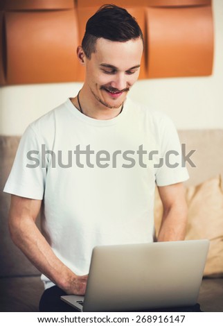 Young business man sitting on a sofa, relaxing and doing freelance work with a laptop at his new home