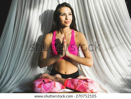 Young dark-haired athletic sporty slim woman doing yoga exercise Lotus pose with namaste hands at home while the sunset