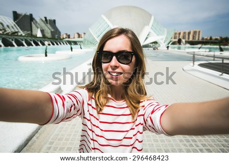 Happy urban teenage girl traveler takes selfie self portrait photo with smart phone camera while travel in Valencia, Spain