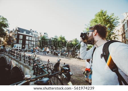 Happy stylish photographer taking a photo of Amsterdam canals, Netherlands. Student travels abroad and takes pictures for his blog.