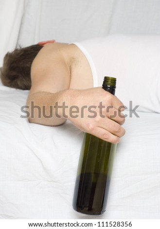Drunk man passed out in the bed with a wine bottle in his hand.