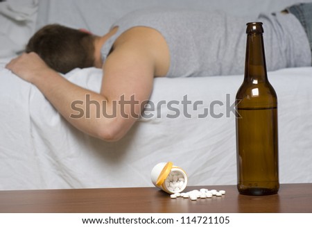 Beer bottle and pills on the table. Man sleeping on the sofa.