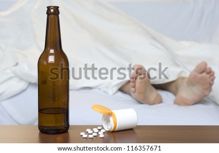 Beer bottle and pills on the table. Person sleeping in the background.