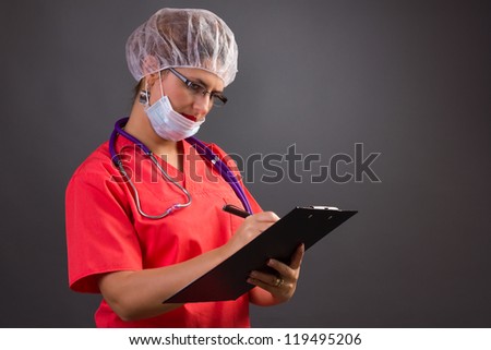 Female doctor with cap and mask writing on clipboard isolated on grey background