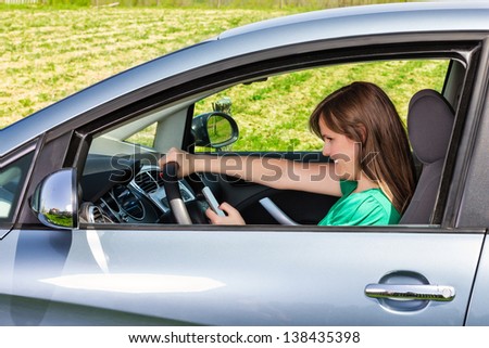 Smiling young woman driver reading/typing a text message on her mobil phone