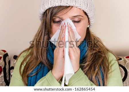 Young woman blowing her nose, feeling bad, at home