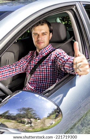 Happy young man with thumb up at the wheel of his car