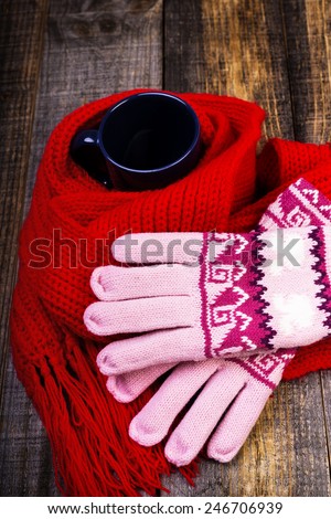 Cup of hot drink wrapped by red scarf and gloves on wooden board.Closeup
