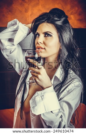 Sensual brunette young woman in  man\'s shirt  holding a glass of wine in the bedroom
