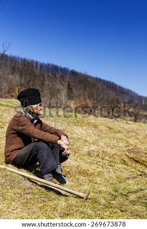 Old man with hat having a break from work, resting on the field