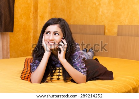 Happy beautiful teenage girl speaking on her smart phone on the bed