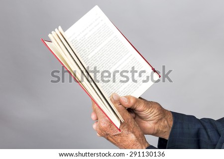 Closeup of old man hands holding an open book over gray background