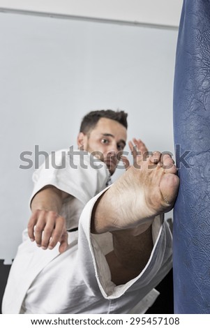 Athletic karate fighter giving a forceful foot kick to a heavy bag during his training