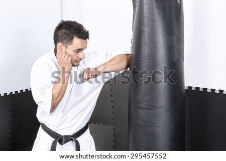 Young man in kimono throwing punches at a heavy punching bag during his training