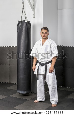 Portrait of athletic black belt karate man standing next to a boxing bag