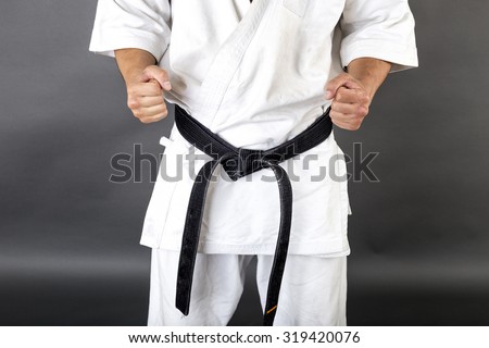 Young man in white kimono and black belt training martial art over gray background