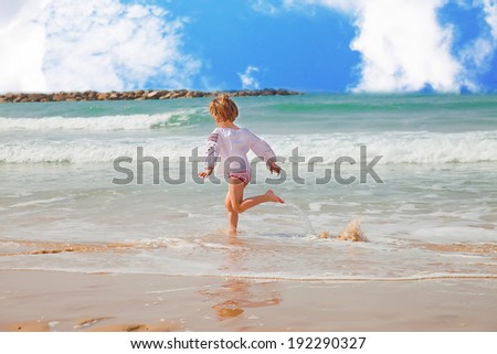 Girl running along the surf line splashing water