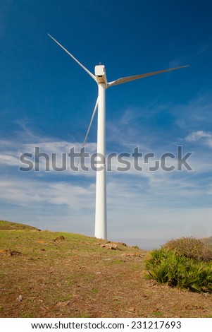 Single windmill producing electrical power on a hill against deep blue sky