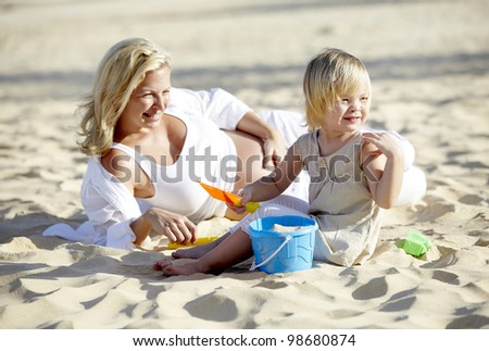 a pregnant mother plays sand with her daughter