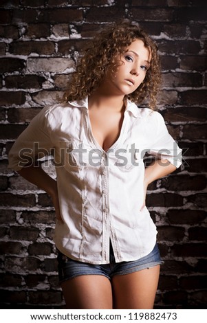 Beautiful young curly hair woman wearing white shirt on brick wall background. Fashion portrait.