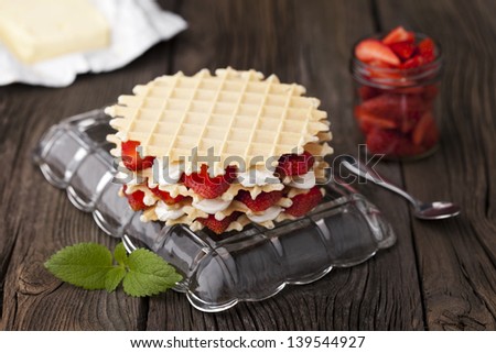 Traditional homemade fresh baked waffles served with strawberries and whipped cream. Dessert and fresh ingredients composition.