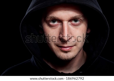 Young curly hair caucasian man wearing black hooded sweatshirt. Low key portrait taken on black background.